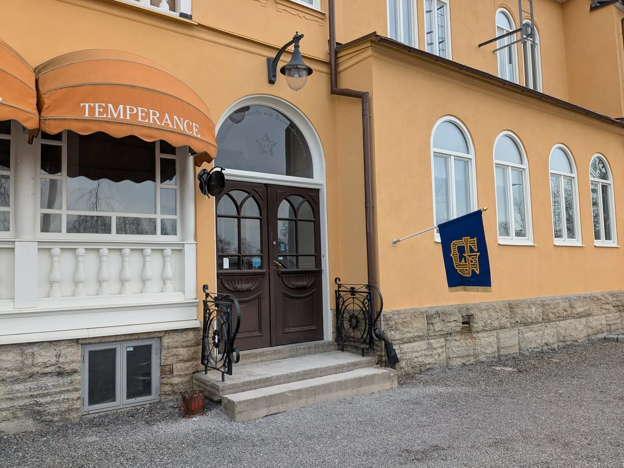 Entrén till Temperance: bruna pardörrar, orange markis och Gillesflaggan i blått och guld på väggen.